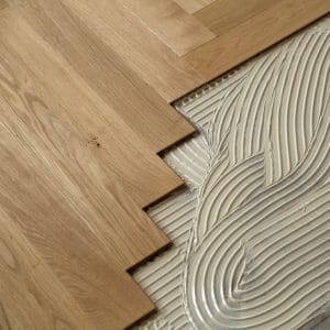 Installation d'un parquet en bois naturel avec de la colle adhésive structurée, appliquée sur le sol pour fixer les lames de bois.