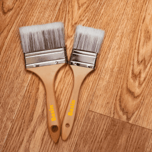 Deux pinceaux en bois de la marque Basin, de tailles différentes, posés sur un parquet en chêne, idéaux pour appliquer des huiles ou vernis pour la protection et l’entretien du bois.
